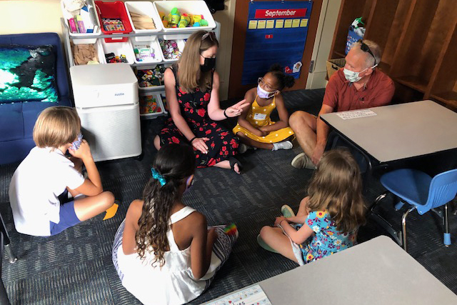 Jon Green seated on the floor of a classroom along with new Hamilton students and a teacher.