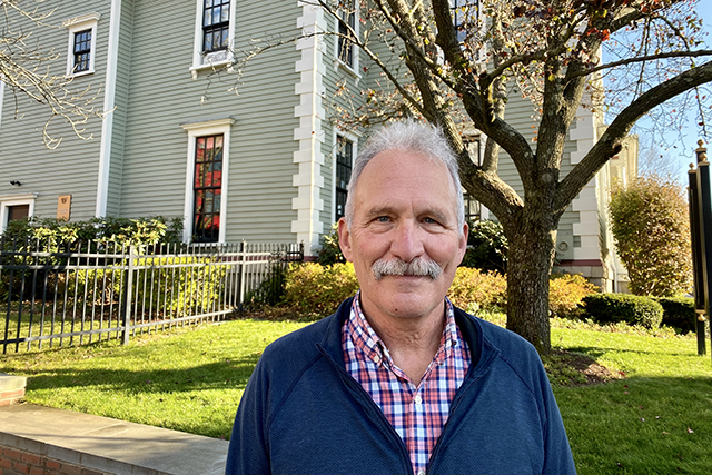 Jon Green stands in front of The Hamilton School building and smiles at the camera.