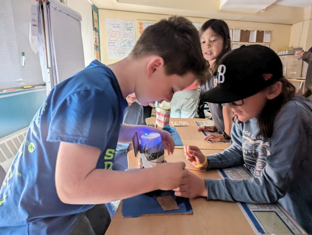 Third-grade students building a lighthouse in Wheeler's DIB Lab. The light at the top of the model lighthouse is on and three students are looking at it.