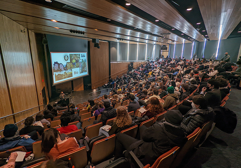Upper School students gathered in an auditorium listening to a speaker at the front of the room.