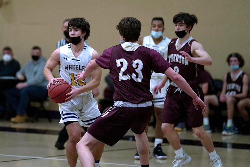Wheeler basketball players on the court against an opposing team. A Wheeler player is looking to pass the ball.