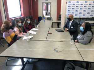 Wheeler students meet with Kyle Bennett and Bonnie Clark of the United Way of Rhode Island in a conference room. Everyone is seated at rectangular tables that are pushed together. A United Way banner is in the background.