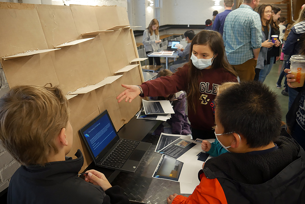 A student extends a hand out to demonstrate an invention to a group of Lower School students at the Design Convention in the Union.