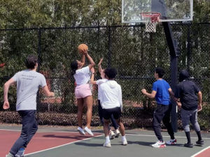 Wheeler students play basketball on an outdoor court. One student is in the motion of shooting at the basket.