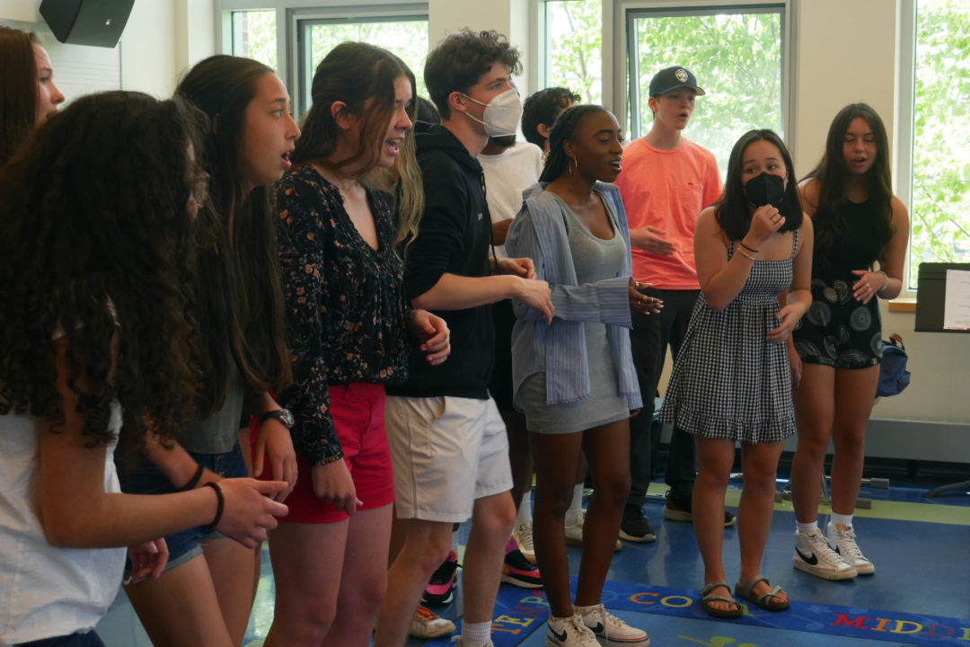 Members of the 18-Wheeler a capella group sing alongside one another in a classroom.
