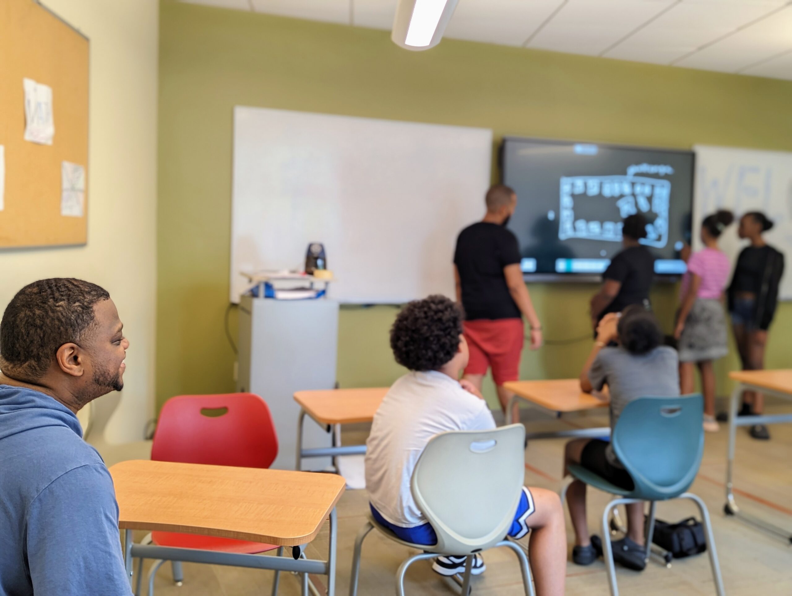 Photo of Mr. Davis in focus as he watches a lesson with Breakthrough Providence students and their teacher in a classroom.