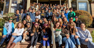Members of the Class of 2024 sitting on the steps of Baker House while wearing "2024" glasses and smiling at the camera.