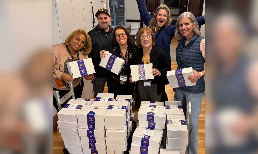 Members of the Enrollment and Operations team smiling and posing at the camera with a cart full of packages of acceptance letters.