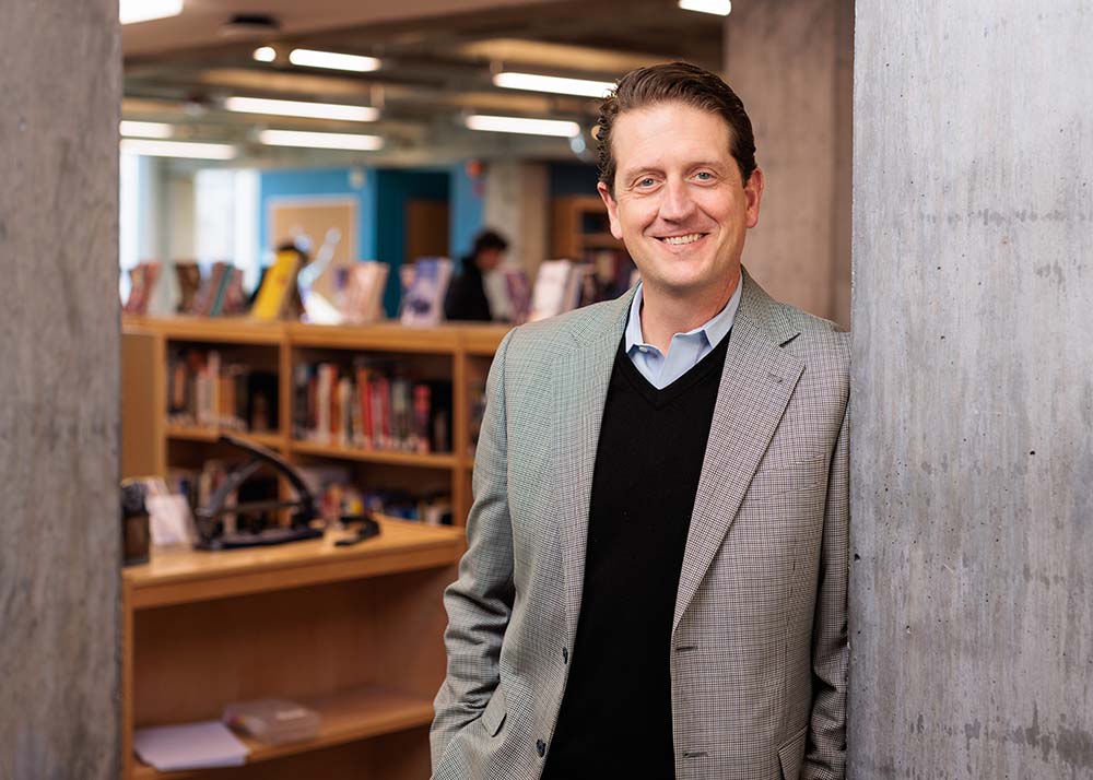 Head of School Mark Anderson standing in Prescott Library. He's smiling while looking towards the camera.