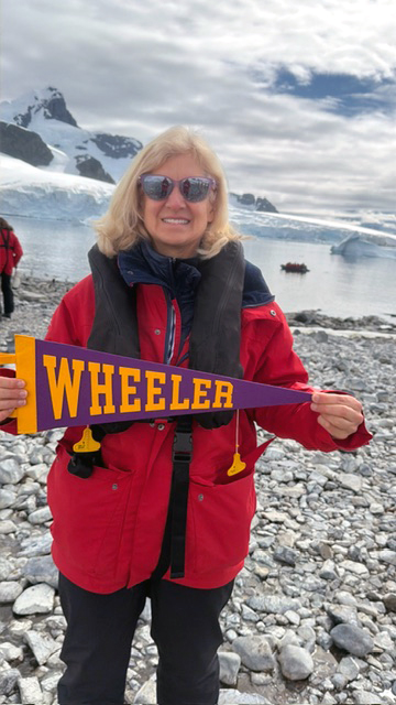 Wilson stands in Antarctica while holding a Wheeler purple and gold pennant.